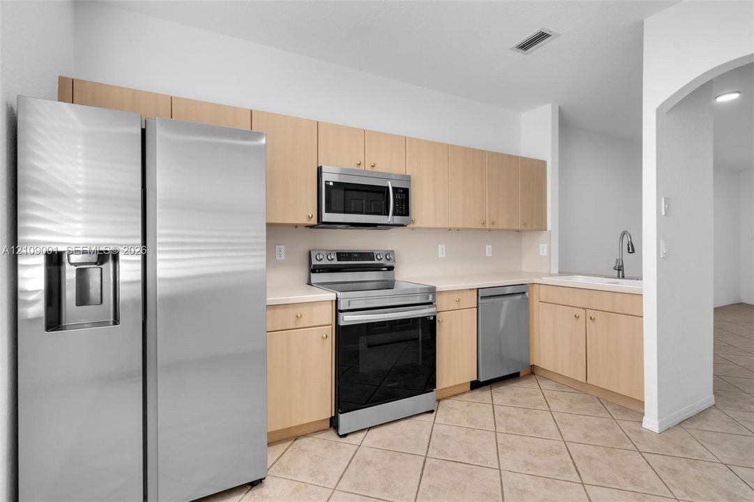 Kitchen featuring stainless steel appliances, wood-finish cabinetry, solid-surface countertops, and diagonal tile flooring