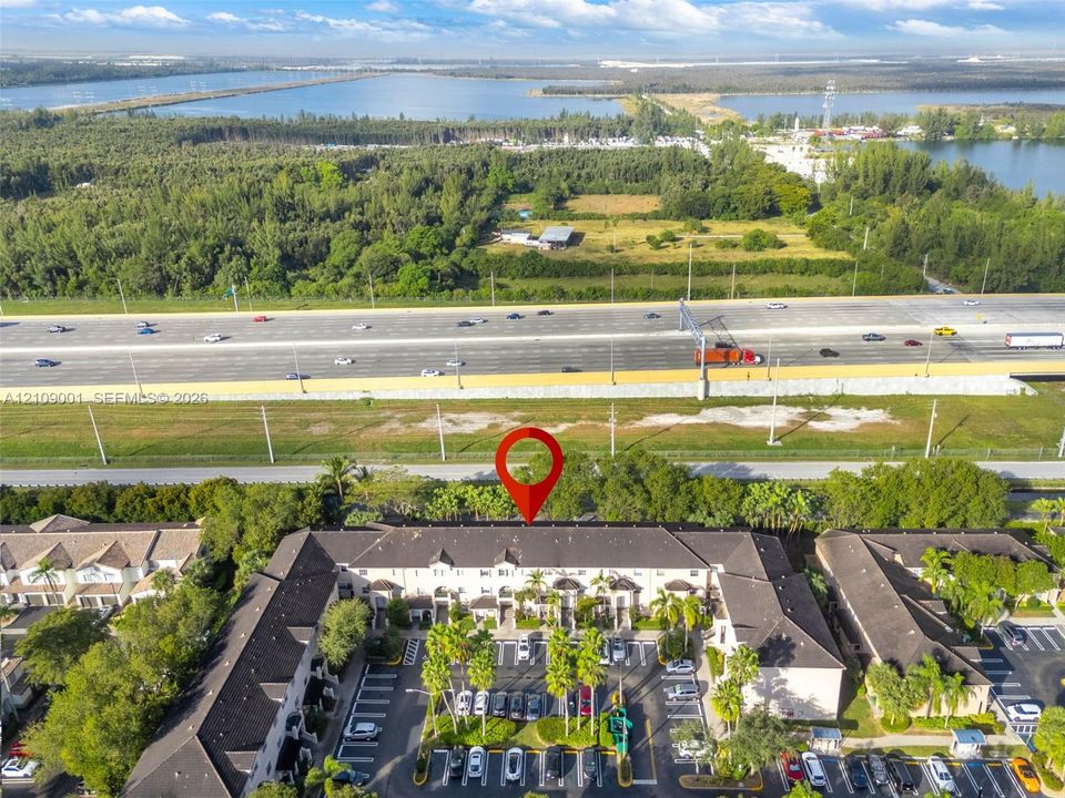 Aerial perspective featuring a multi-story residential building with a pitched shingle roof, integrated surface parking, and manicured landscaping throughout the grounds