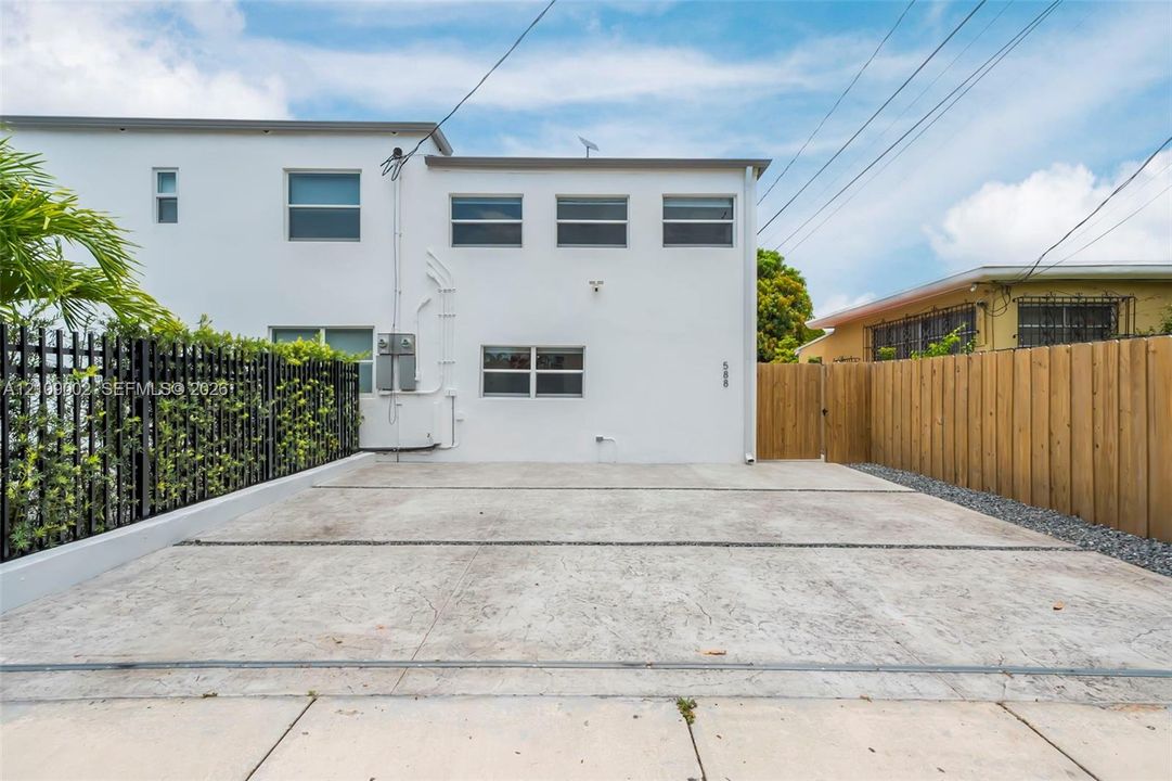 Exterior facade featuring smooth white stucco finish, multi-pane window configurations, dedicated concrete off-street parking area, and vertical wood privacy fencing