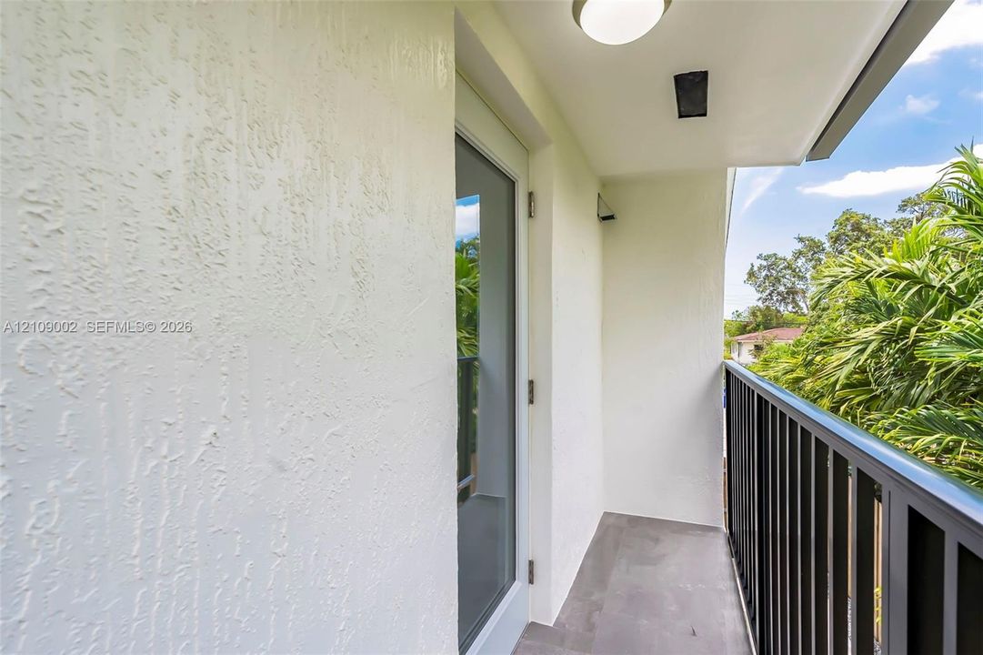 Private balcony featuring textured stucco walls, grey tile flooring, and a black metal railing