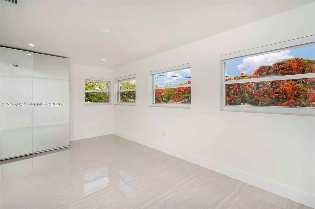 Neutral-toned tile flooring, recessed ceiling lighting, built-in floor-to-ceiling cabinetry with a glossy finish, and multiple windows featuring external scenery