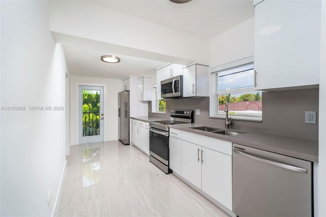 Kitchen featuring white flat-panel cabinetry, stainless steel appliances, solid-surface countertops, and light-toned flooring