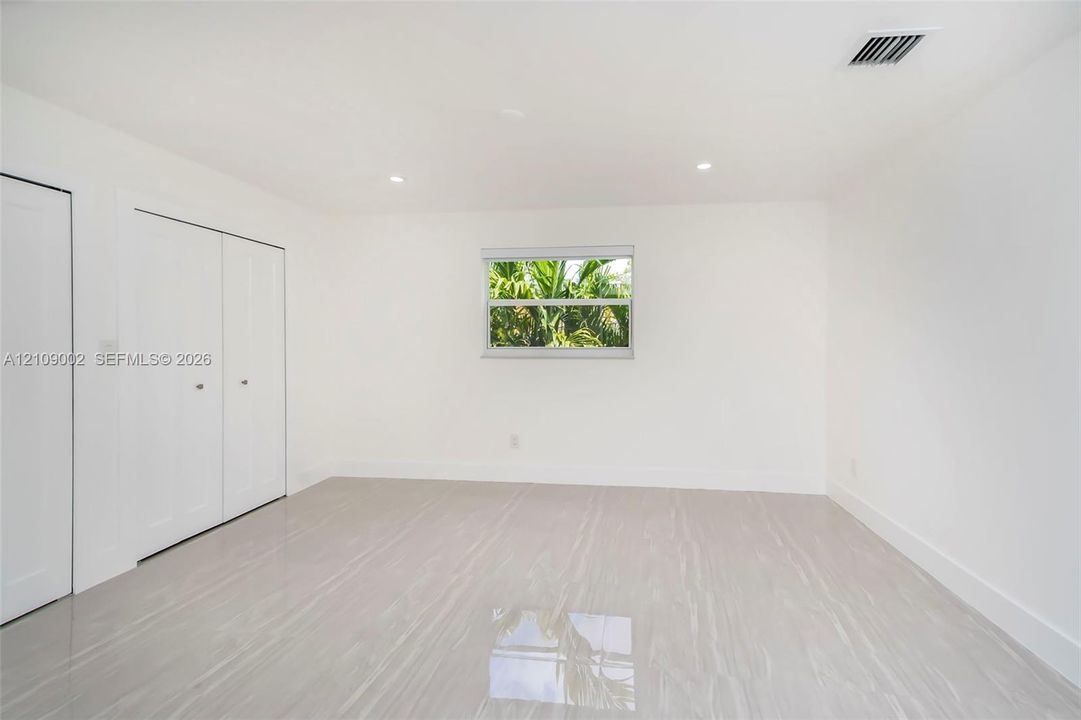 Neutral interior space featuring polished tile flooring, recessed lighting, white walls, and a multi-panel closet with brushed metal hardware