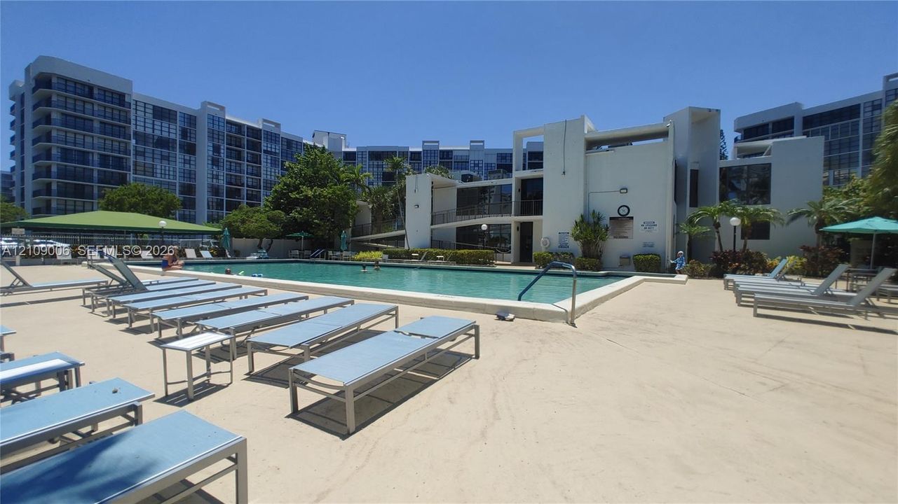 Swimming pool with a concrete pool deck, covered shade structures, and manicured landscaping