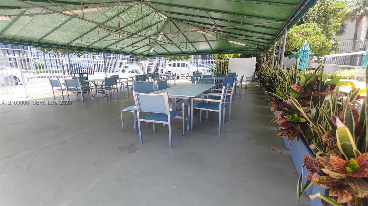 Covered outdoor patio area featuring a metal-frame canopy, smooth concrete flooring, and perimeter metal fencing