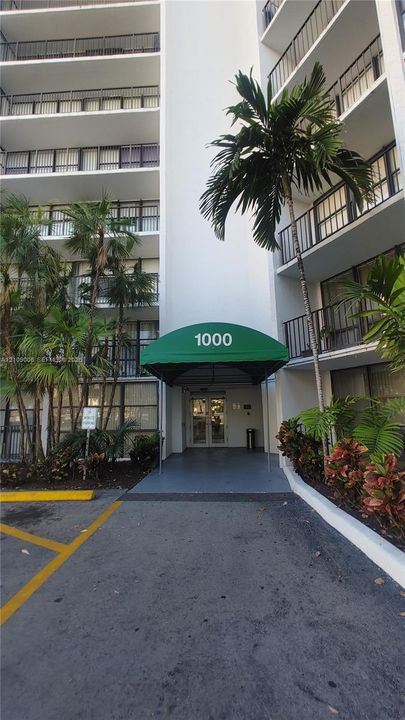 High-rise exterior featuring private balconies, a covered entrance with a green awning, and established tropical landscaping