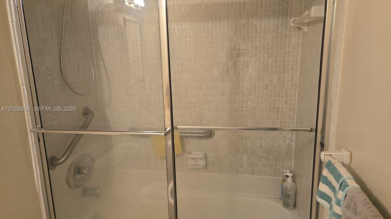 Shower and tub combination featuring sliding glass doors, a small-format tiled surround, and chrome hardware including mounted grab bars
