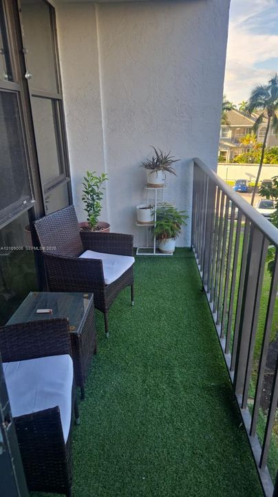 Covered balcony featuring artificial turf flooring, a metal railing, and textured wall finishes