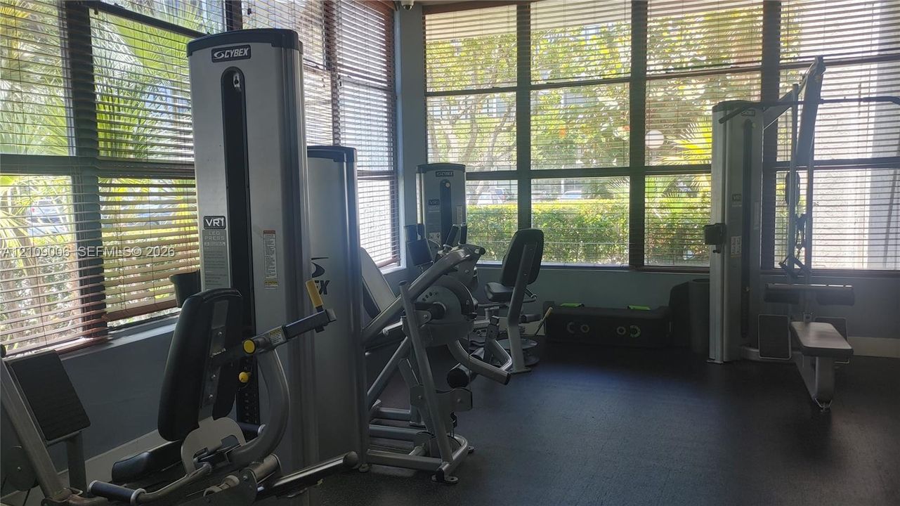 Multi-purpose fitness room featuring wall-to-wall windows, adjustable slatted blinds, and rubberized flooring