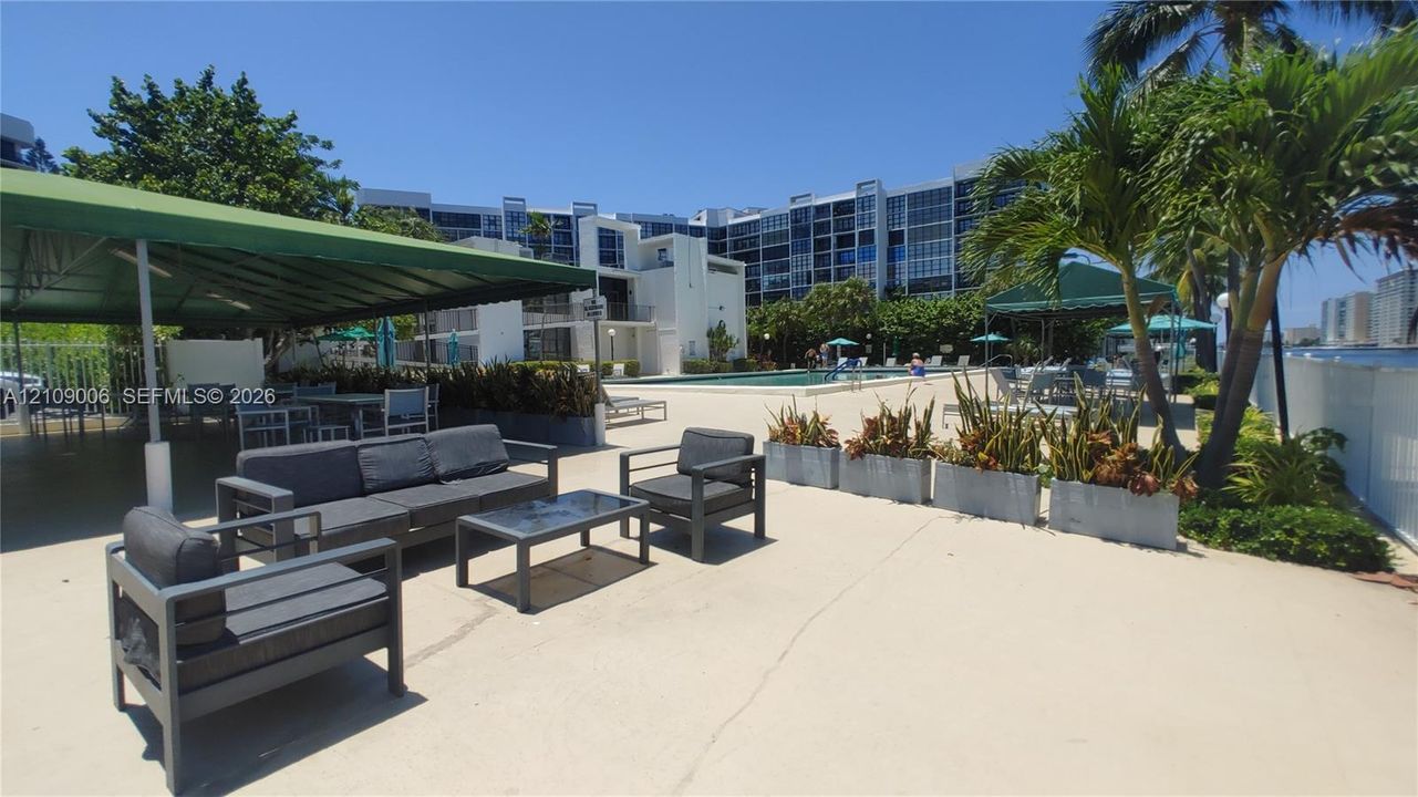 Outdoor swimming pool featuring a concrete deck, covered pavilion, built-in planters, and mature palm trees