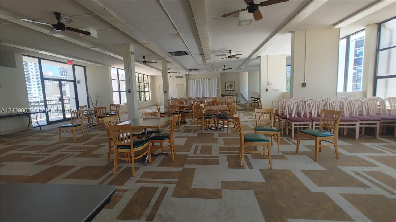 Expansive interior space featuring patterned carpeting, multiple ceiling fans, floor-to-ceiling window panels, and neutral wall tones