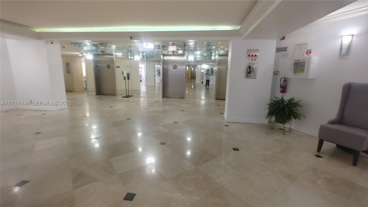 Lobby featuring polished stone flooring with inlaid tile accents, stainless steel elevator doors, mirrored wall paneling, and recessed ceiling lighting