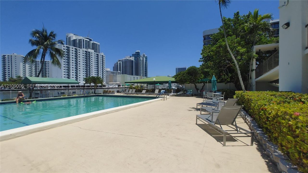 Outdoor swimming pool with a concrete pool deck, green awnings, and manicured privacy hedges