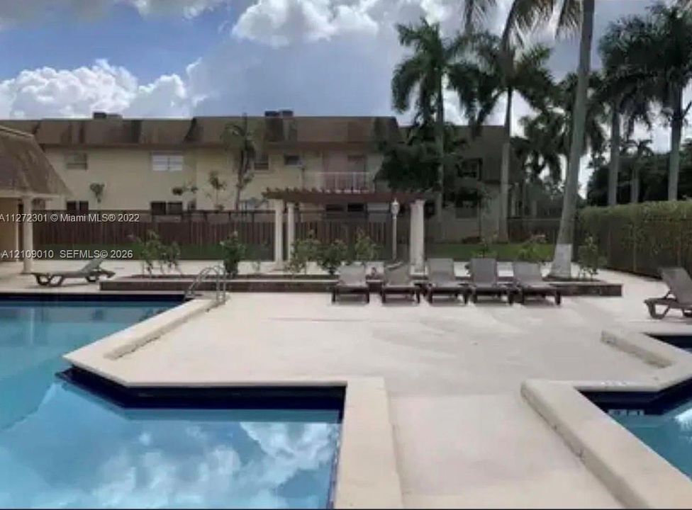 Swimming pool area featuring a paved deck, pergola with columns, and mature palm trees