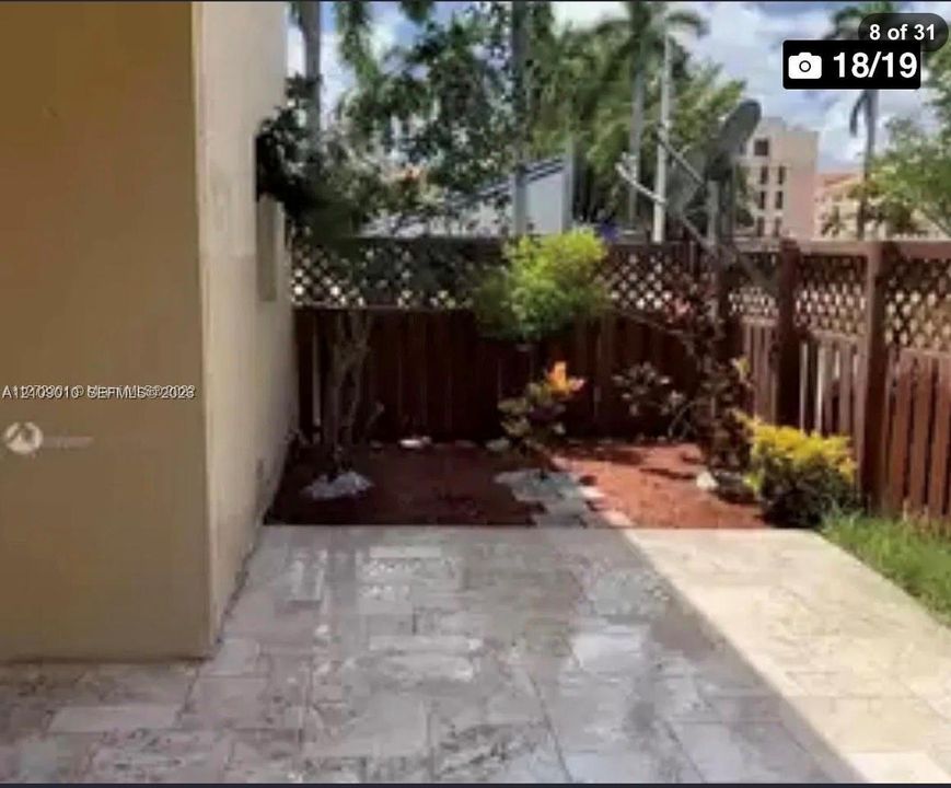 Enclosed patio featuring natural stone flooring, mulch garden beds, and privacy lattice fencing