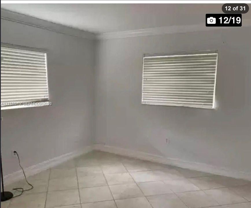 Neutral-toned interior featuring large-format diagonal tile flooring, crown molding, and two windows with horizontal blinds