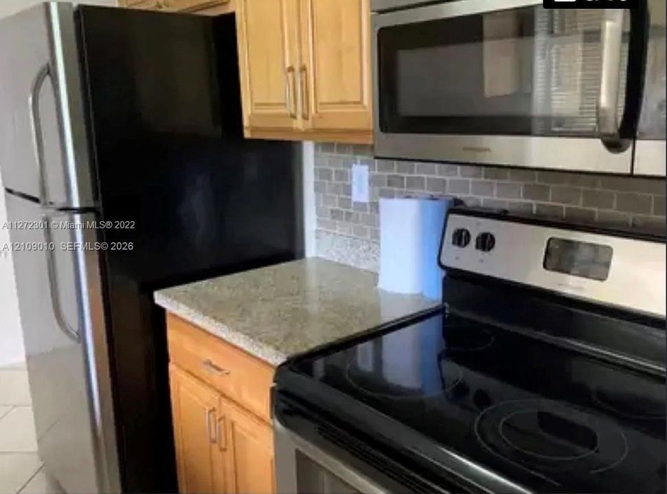 Kitchen featuring shaker-style wood cabinetry, natural stone countertops, a tiled backsplash, and stainless steel appliances