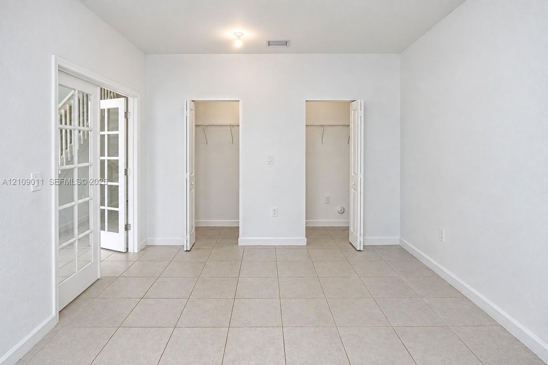 Neutral-toned tile flooring, dual reach-in closets with shelving, and multi-pane glass French doors