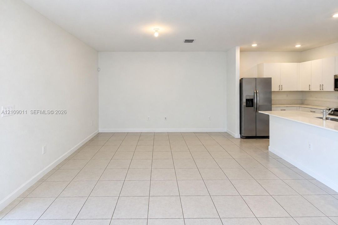 Open-concept floor plan featuring ceramic tile flooring, white flat-panel cabinetry, quartz countertops, and stainless steel appliances