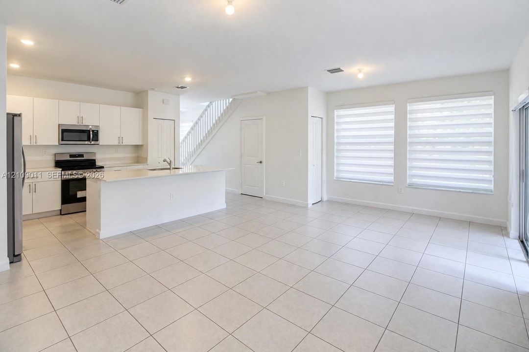 Open-concept kitchen featuring white cabinetry, a center island with a quartz countertop, stainless steel appliances, ceramic tile flooring, and dual-pane windows with light-filtering blinds