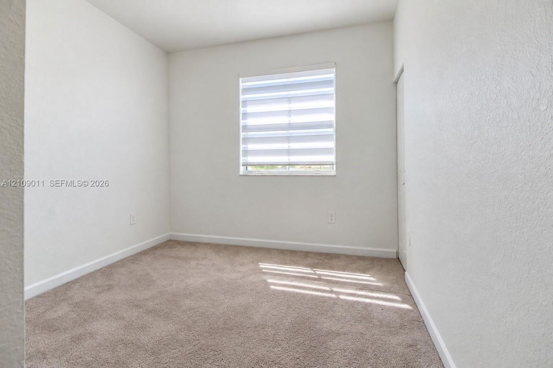 Neutral-toned wall-to-wall carpeting and a single-hung window featuring adjustable dual-layer shade treatments
