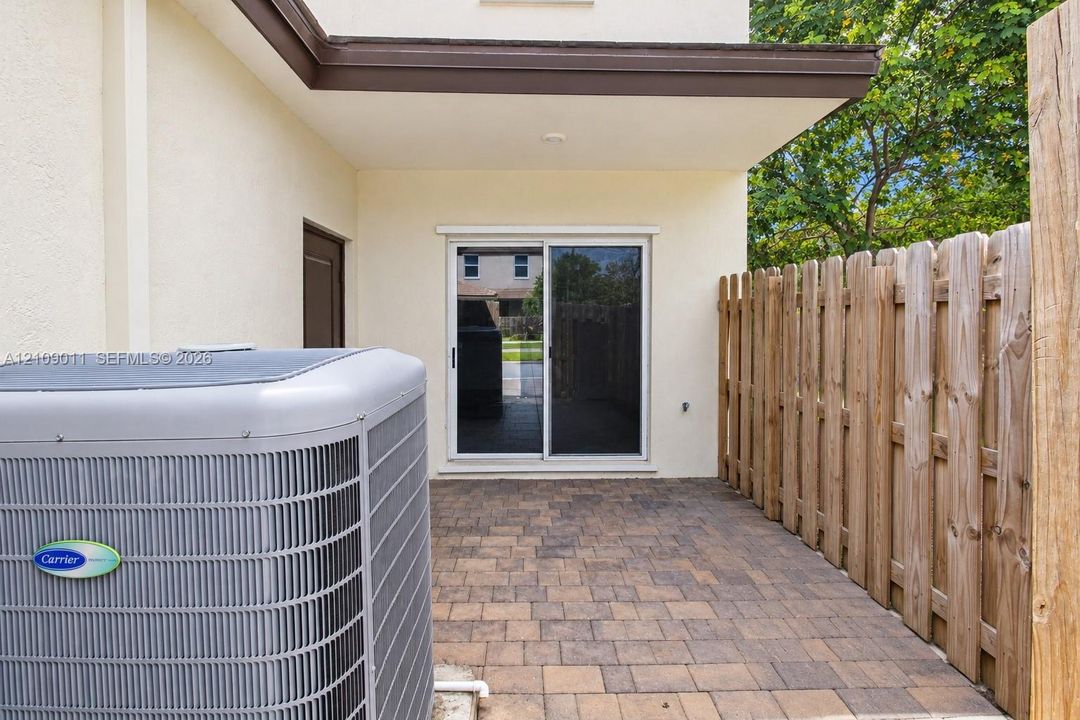 Exterior patio featuring paved stone flooring, a wood privacy fence, and a sliding glass door