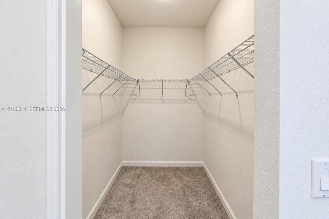 Walk-in storage space featuring neutral carpeting and tiered white wire shelving