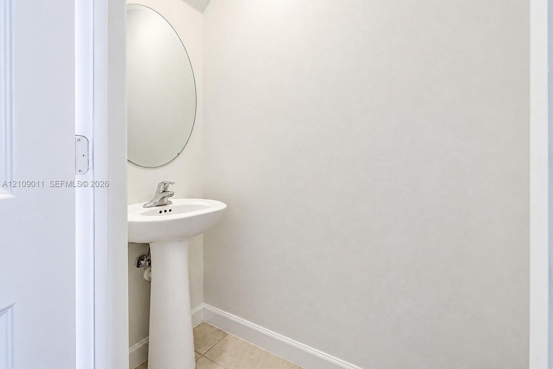 White pedestal sink with a polished chrome faucet, oval wall-mounted mirror, and tile flooring