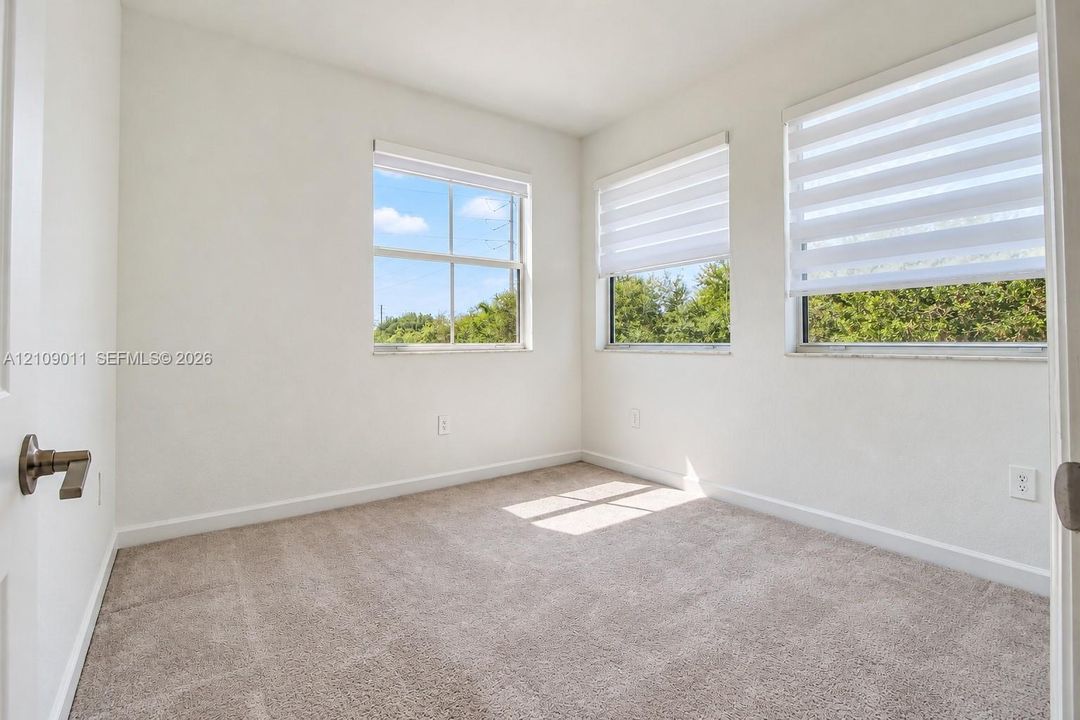 Neutral-toned carpeting, triple-window configuration, and dual-layered window shades