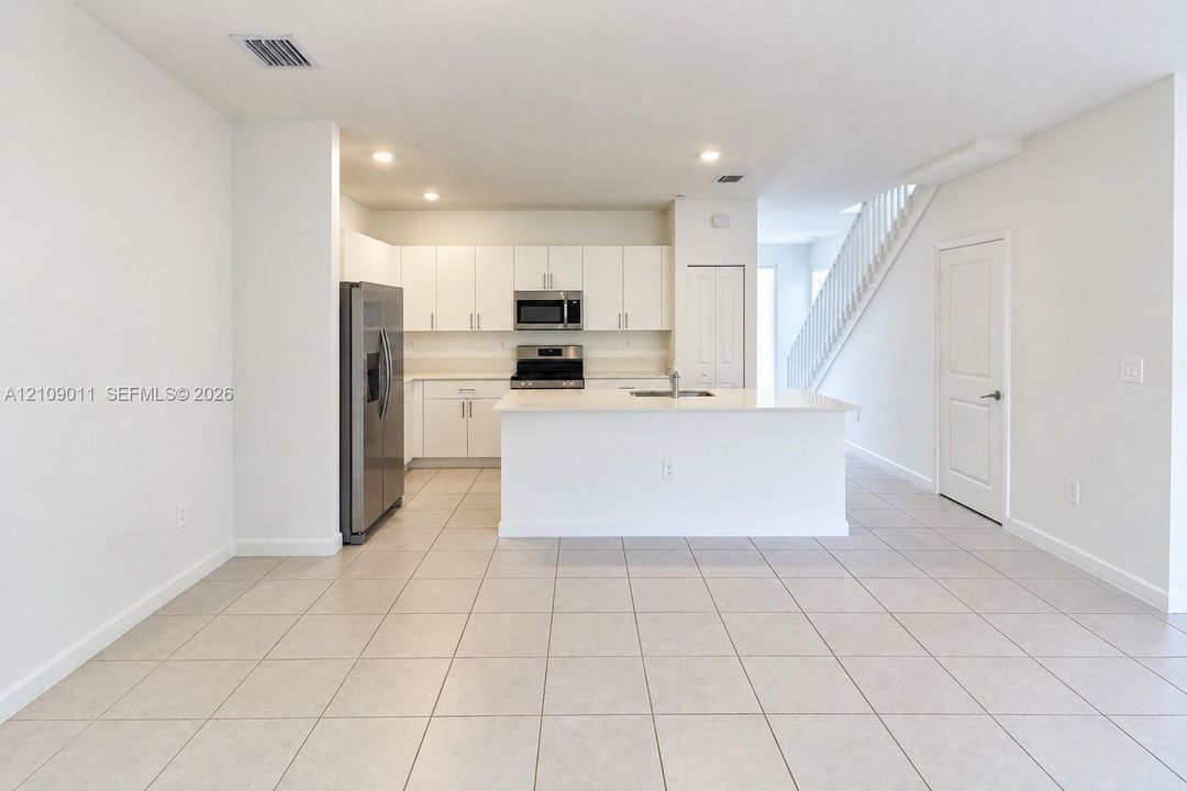 Kitchen featuring white cabinetry, an island with a sink, stainless steel appliances, and tile flooring