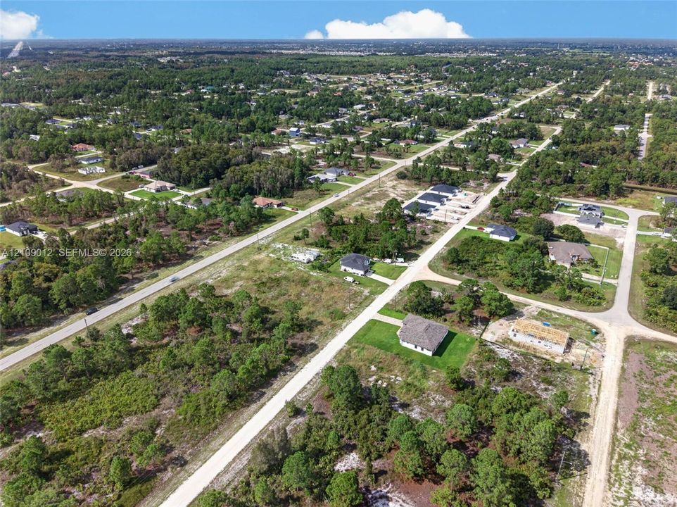 Aerial perspective of a corner lot situated in a low-density residential area, featuring native vegetation and direct access to paved and unpaved roadway infrastructure