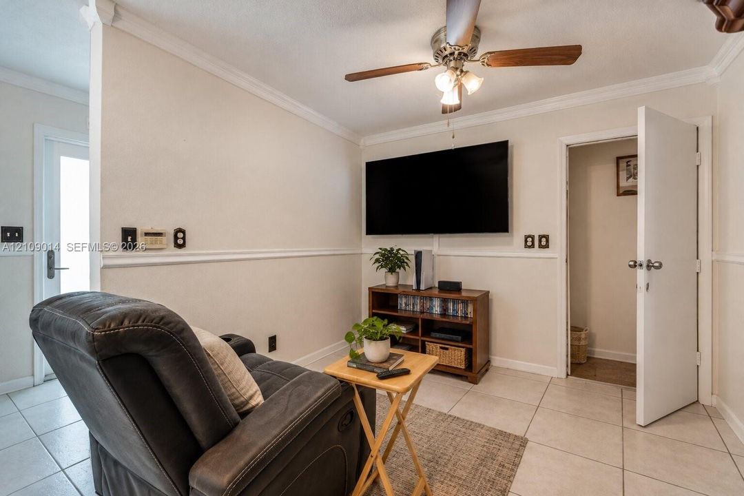 Interior room featuring neutral wall paint, chair rail molding, crown molding, large-format tile flooring, and a ceiling fan with light fixture