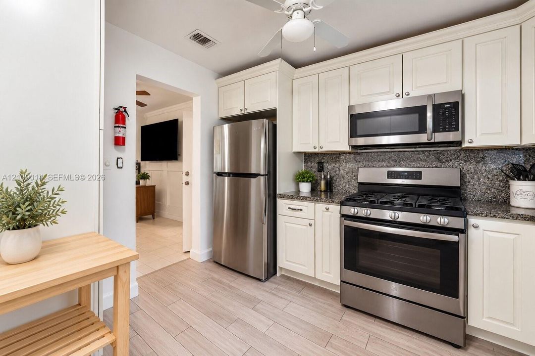 Kitchen featuring shaker-style cabinetry, stone-finish countertops, stainless steel gas range, over-the-range microwave, and wood-finish flooring