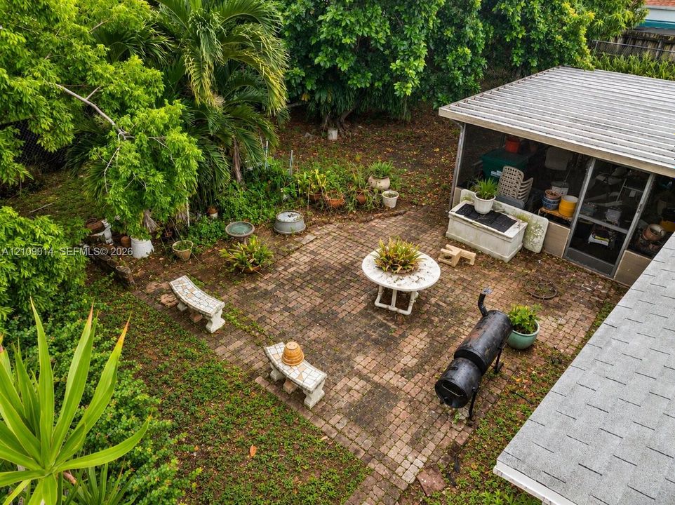 Brick-paved patio featuring a screened-in enclosure, mature landscaping, and shaded canopy trees