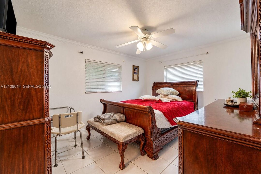 Room featuring neutral wall finishes, tile flooring, crown molding, a central ceiling fan with integrated lighting, and two windows with horizontal blinds