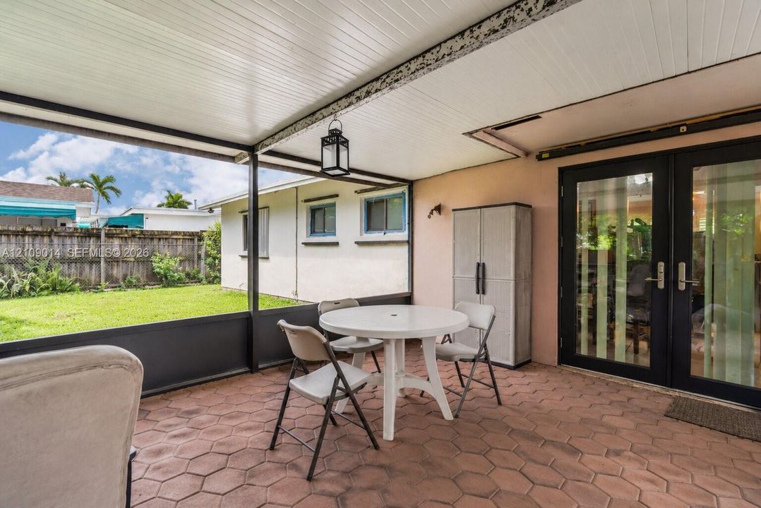 Covered patio featuring hexagonal paver flooring, black-framed screened enclosure, ceiling-mounted lantern light fixture, and black-framed double glass doors