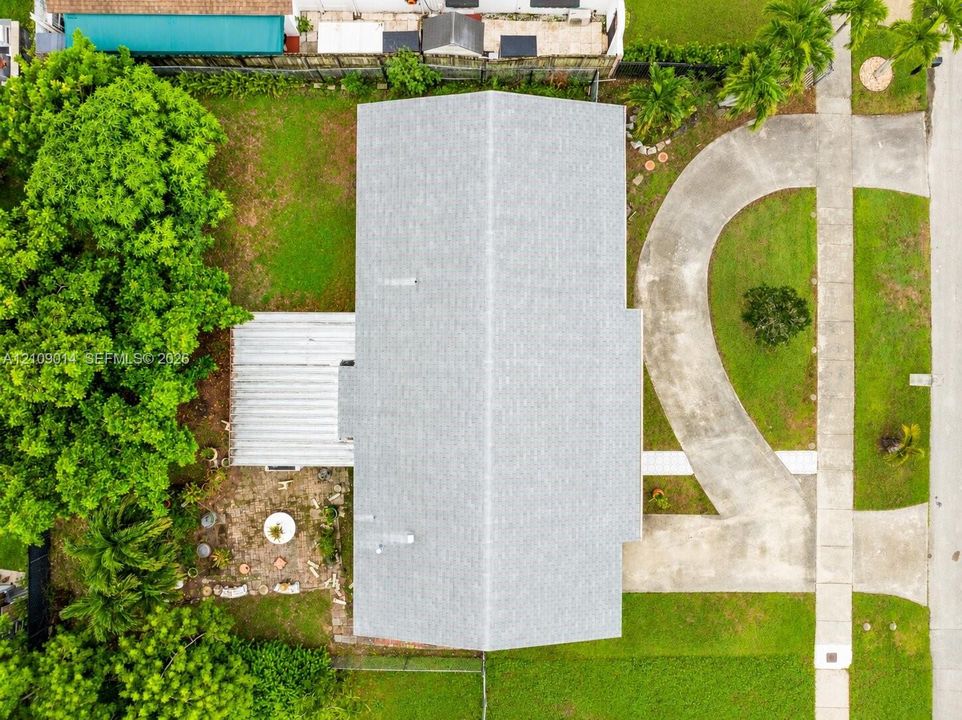 Aerial perspective featuring a shingled roof, a paved circular driveway, a covered rear patio, and mature landscaping