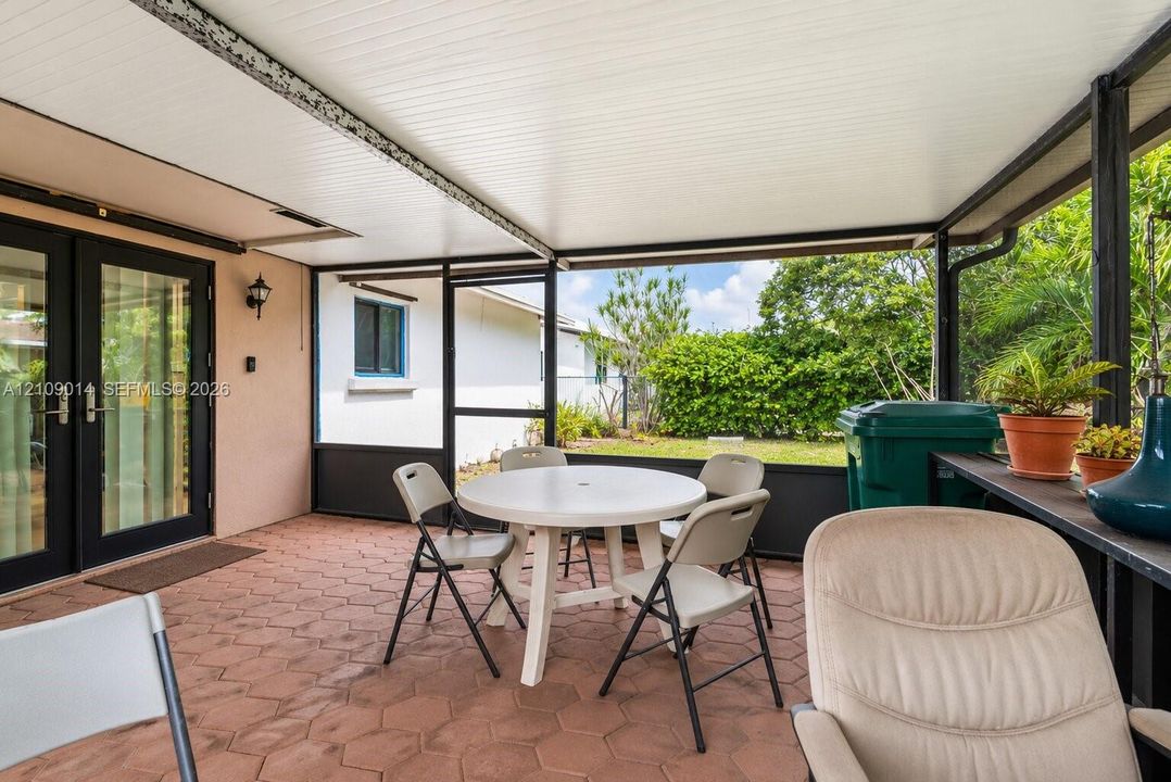 Screened-in patio featuring hexagonal paver flooring, a solid panel roof, and black-framed exterior French doors with glass panes