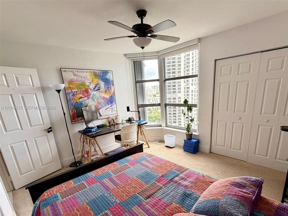Bay window with floor-to-ceiling glass, neutral carpeting, ceiling fan with integrated light fixture, and white dual-panel closet doors