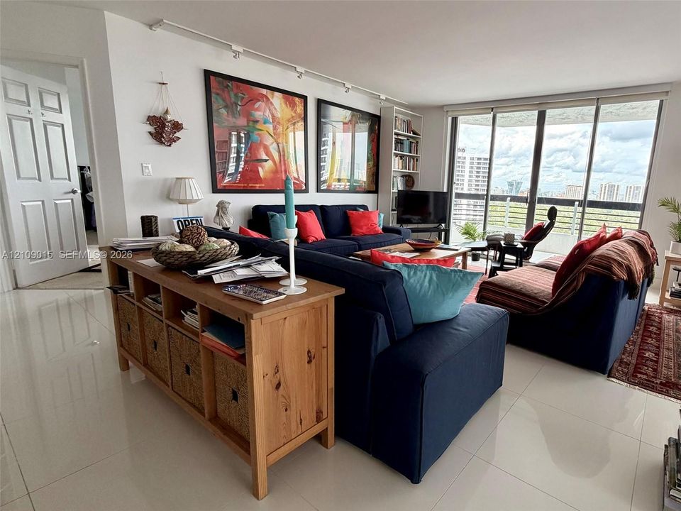 Living space featuring large-format tile flooring, floor-to-ceiling glass doors, integrated track lighting, and built-in shelving