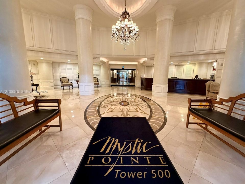 Grand lobby featuring high ceilings with architectural columns, stone tile flooring with decorative medallion inlay, and an ornate crystal chandelier