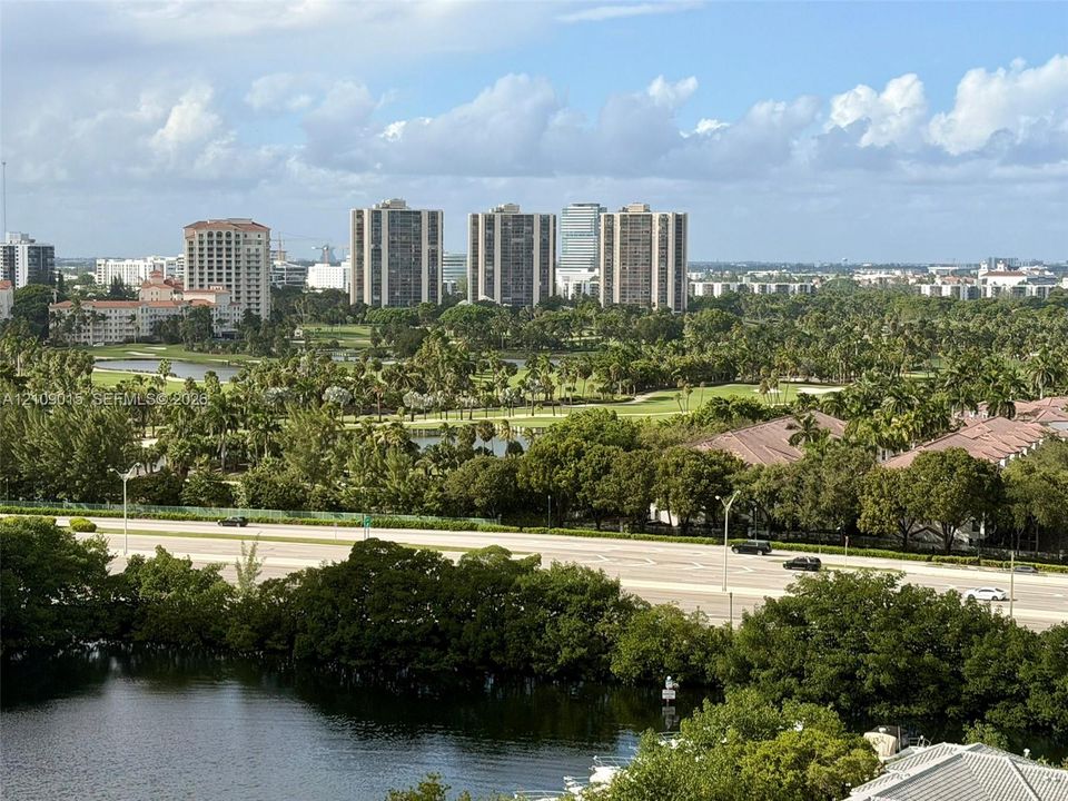 Panoramic landscape featuring golf course grounds, mature tree canopy, natural water features, and high-rise skyline