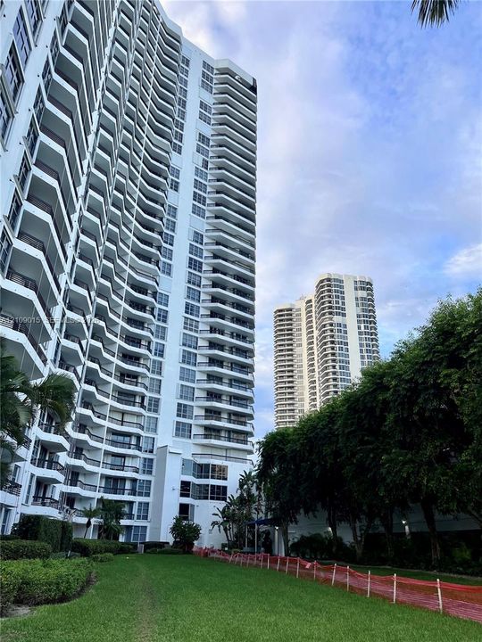High-rise residential exterior featuring expansive private balconies, white facade, and lush surrounding green space