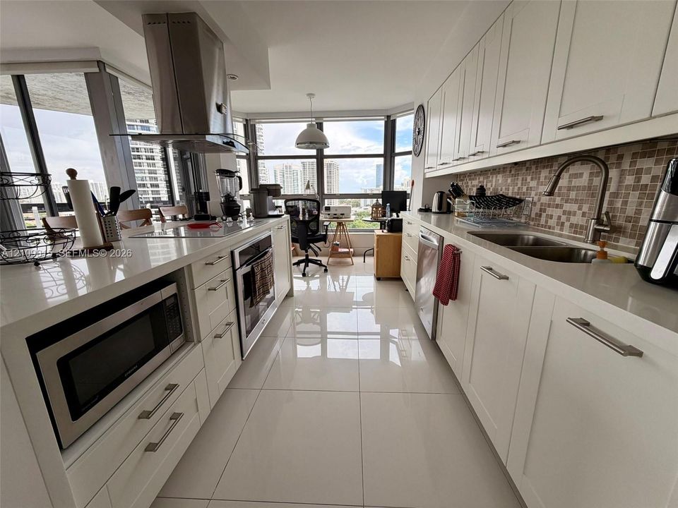 Kitchen featuring white cabinetry, quartz countertops, stainless steel appliances, a mosaic tile backsplash, and large-format porcelain floor tiling