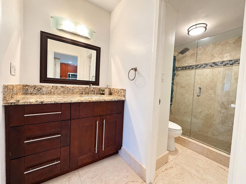 Walk-in shower featuring natural stone wall tile, decorative mosaic glass accent border, frameless glass door, integrated multi-head shower panel, and built-in corner shelving