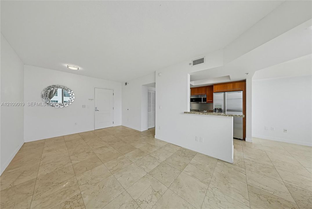 Open-concept interior featuring large-format stone-finish tile flooring, kitchen pass-through with stone countertop, and stainless steel appliances