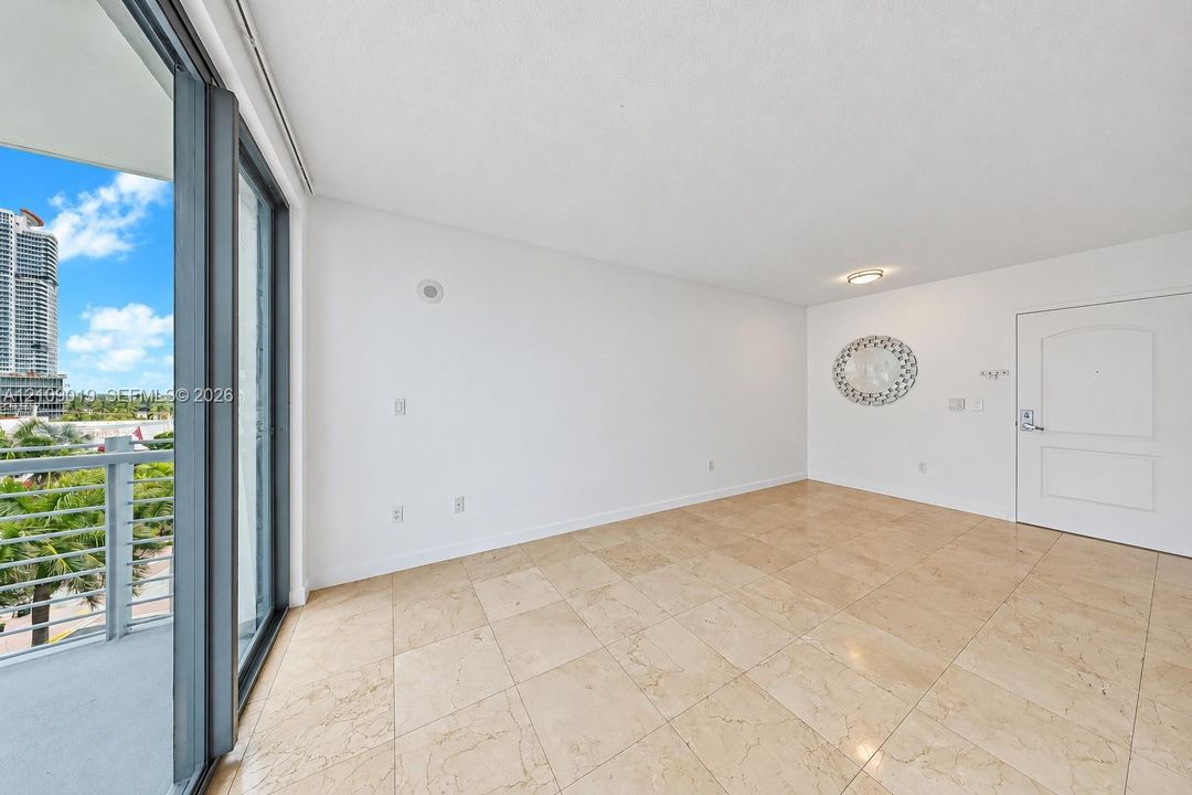 Interior space featuring light-toned stone-finish tile flooring, floor-to-ceiling glass sliding doors, and a private balcony with a metal railing
