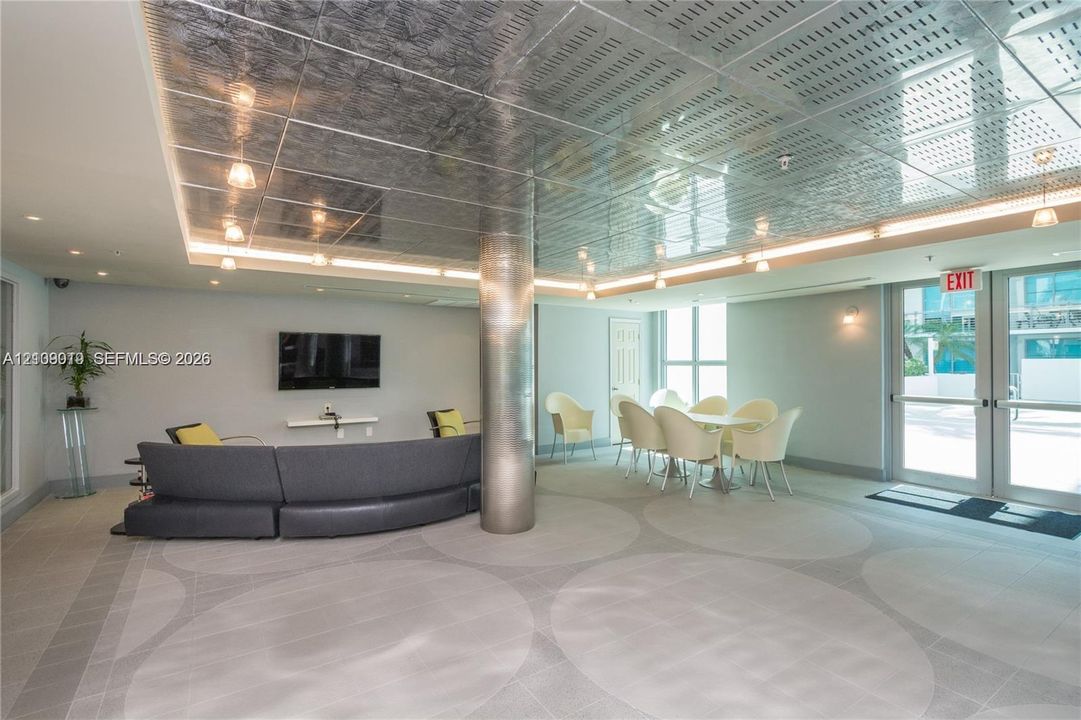 Reflective metallic coffered ceiling with recessed lighting, central brushed-metal structural column, and patterned large-format tile flooring