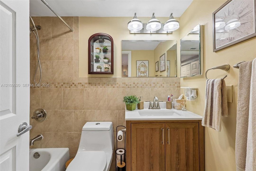 Bathroom featuring a wood-finish vanity with a white countertop, wall-mounted mirrored medicine cabinet, three-light fixture, and a tiled shower surround