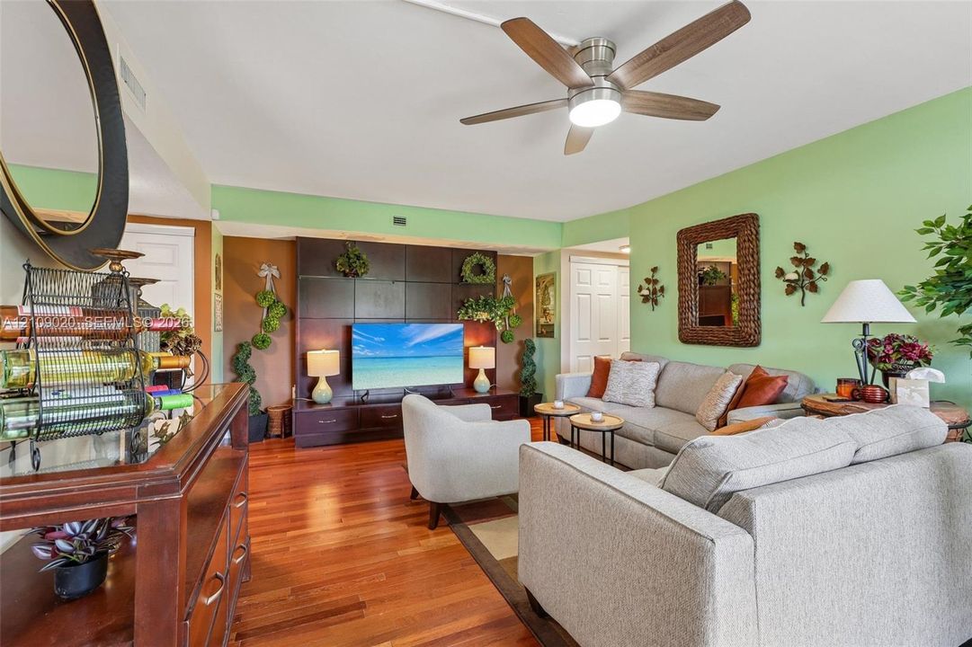 Living area featuring wood-finish flooring, a ceiling fan with integrated lighting, and a dark-toned custom built-in entertainment center
